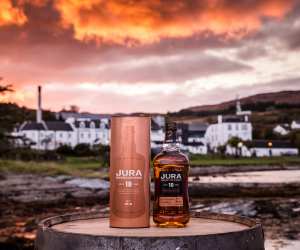 Jura whisky | A bottle of Jura whisky in front of the distillery at sunset